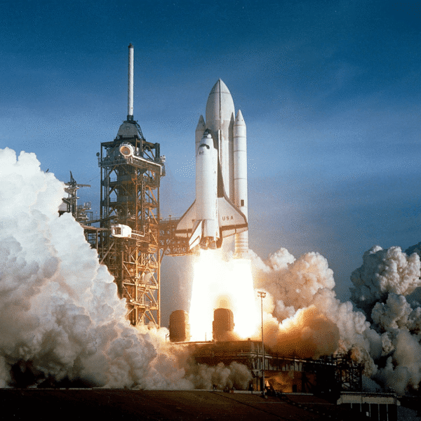Space shuttle launching from pad with fiery booster rockets and smoke against blue sky, symbolizing space exploration and technology advancements.