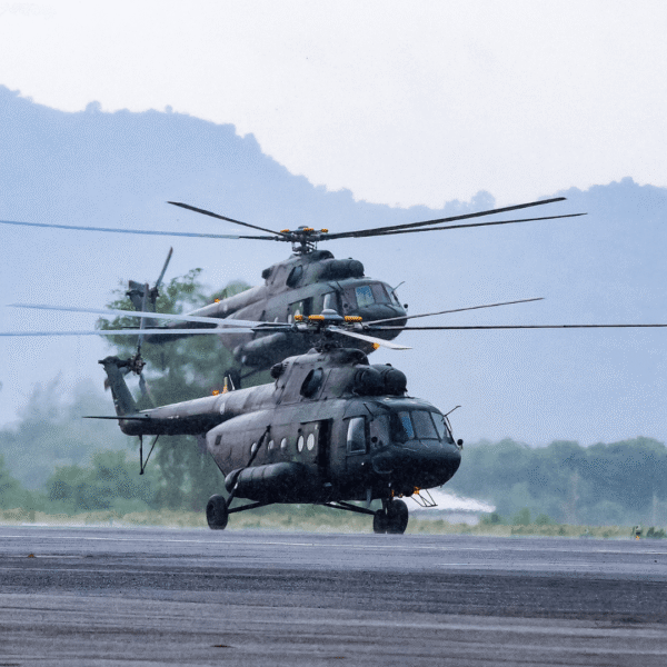 Two military helicopters on a runway with mountains in the background, showcasing aviation power and readiness in a natural setting.