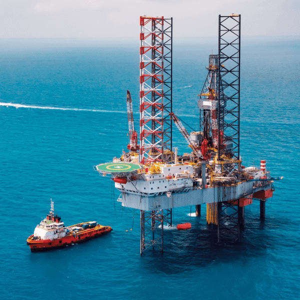 Offshore oil rig in blue ocean with a supply vessel nearby, featuring a helipad and cranes, illustrating maritime industry activities.