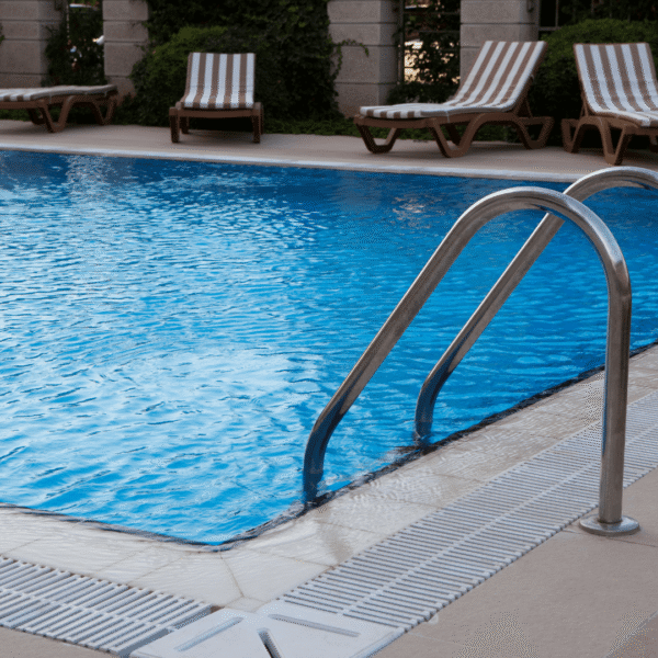 Outdoor pool with clear blue water and metal steps, surrounded by striped lounge chairs and greenery, perfect for relaxation and leisure.