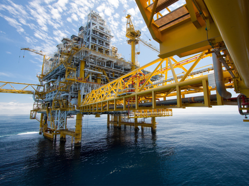 Offshore oil rig with complex machinery and bright yellow structures over the ocean on a clear day.